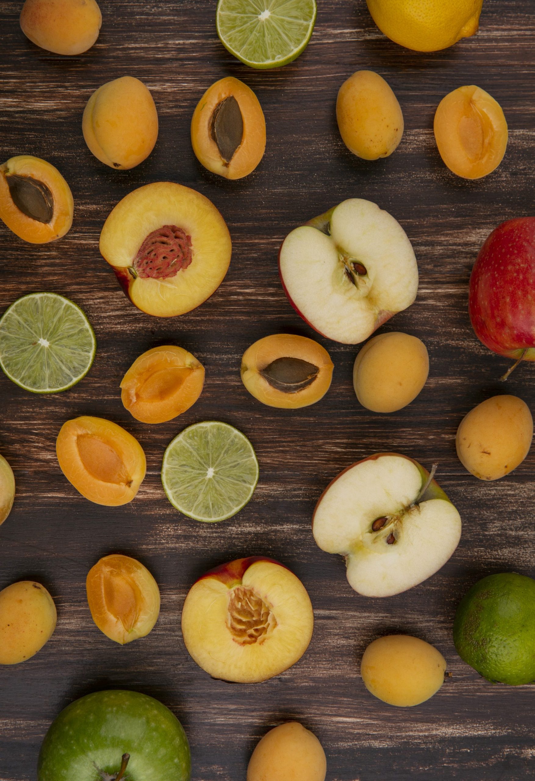 top view halves of a mix of fruits apricots apples peach and lime on a wooden background